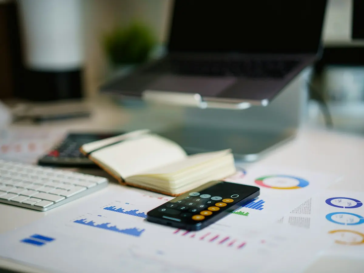 Escritorio con reportes financieros impresos, calculadora y computadora