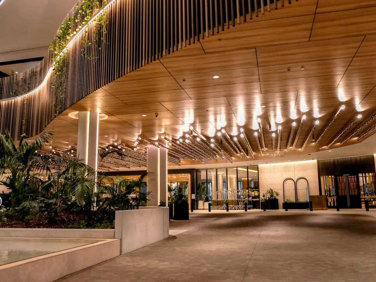 Entrada de un hotel con techo de madera, iluminación cálida y jardineras